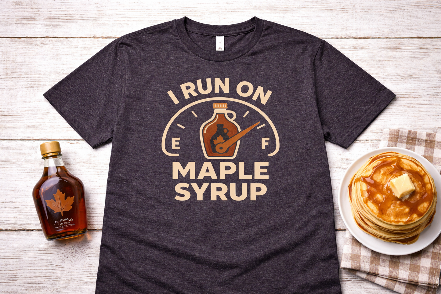 Dark gray t-shirt with 'I Run on Maple Syrup' graphic, bottle of syrup, pancakes, and butter on a wooden surface.