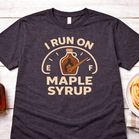 Dark gray t-shirt with 'I Run on Maple Syrup' graphic, bottle of syrup, pancakes, and butter on a wooden surface.